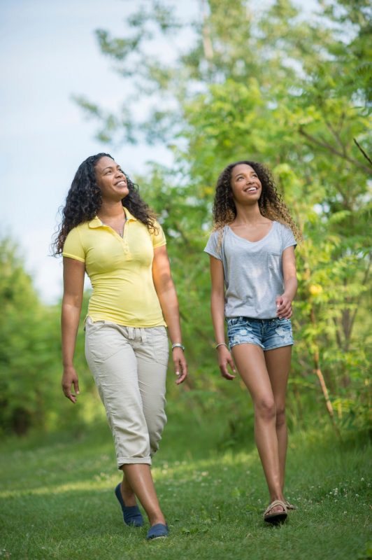 Mother and teenage daughter walking outdoors together, laughing