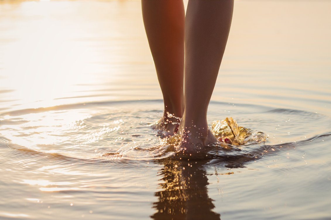 Bare feet standing in shallow water at golden hour